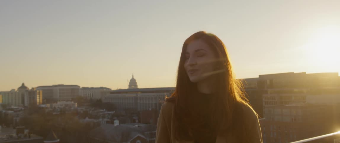 A woman stands on a roof looking at the rising sun