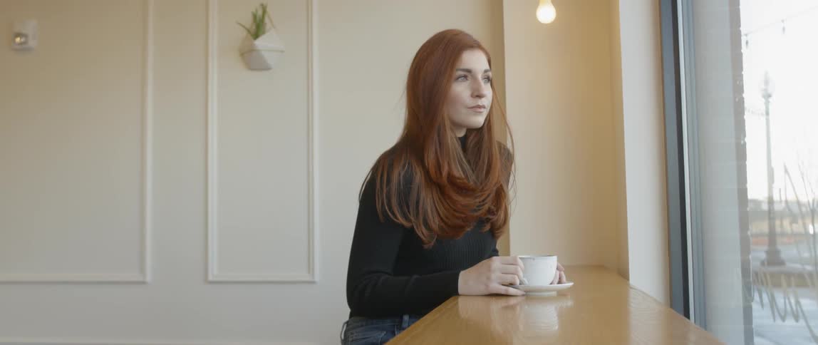 Woman sits at a table holding a teacup