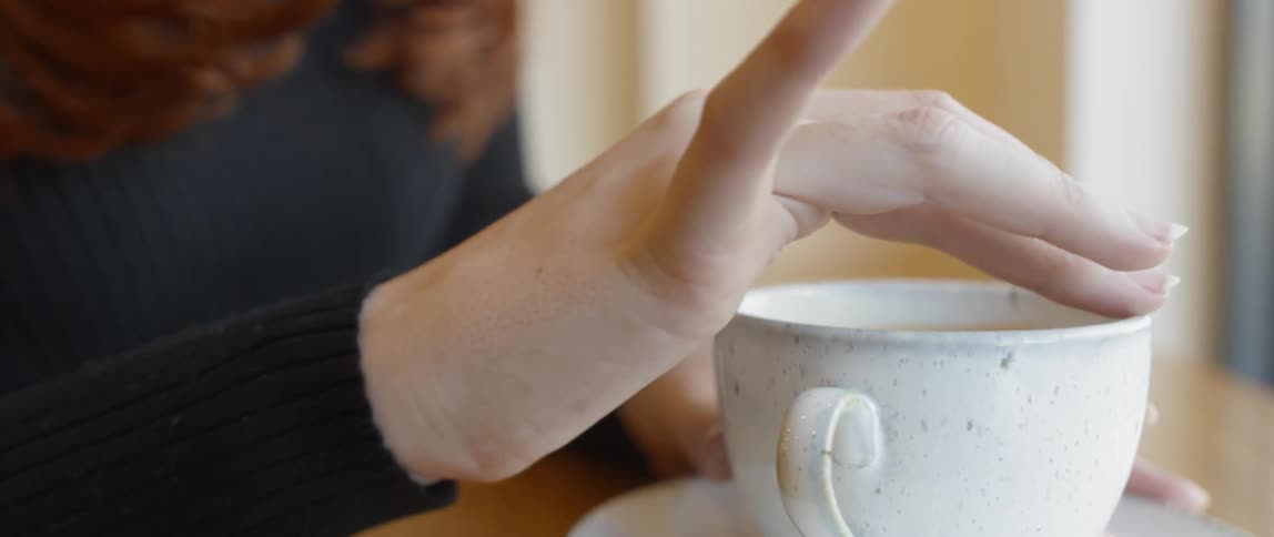 Woman runs her finger around the edge of a tea cup