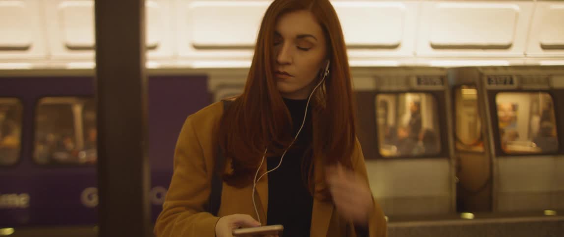A woman puts ear buds on while she waits