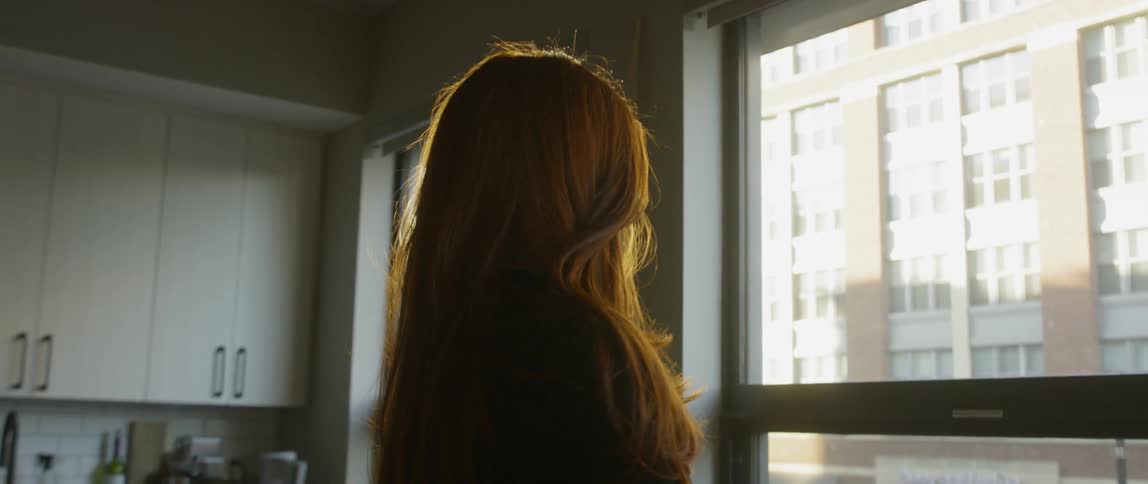 Woman stands in a kitchen looking out the window