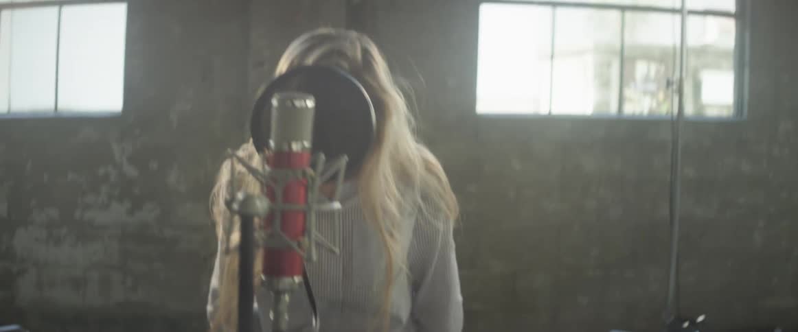 Woman walks in a music studio and sits behind a microphone