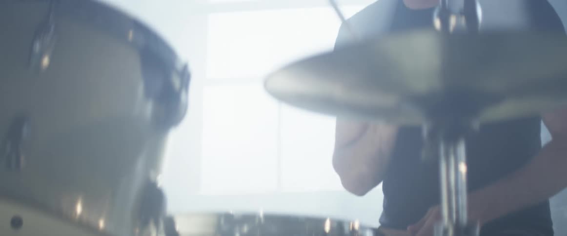 Person plays the drums next to a window with the sun shining in