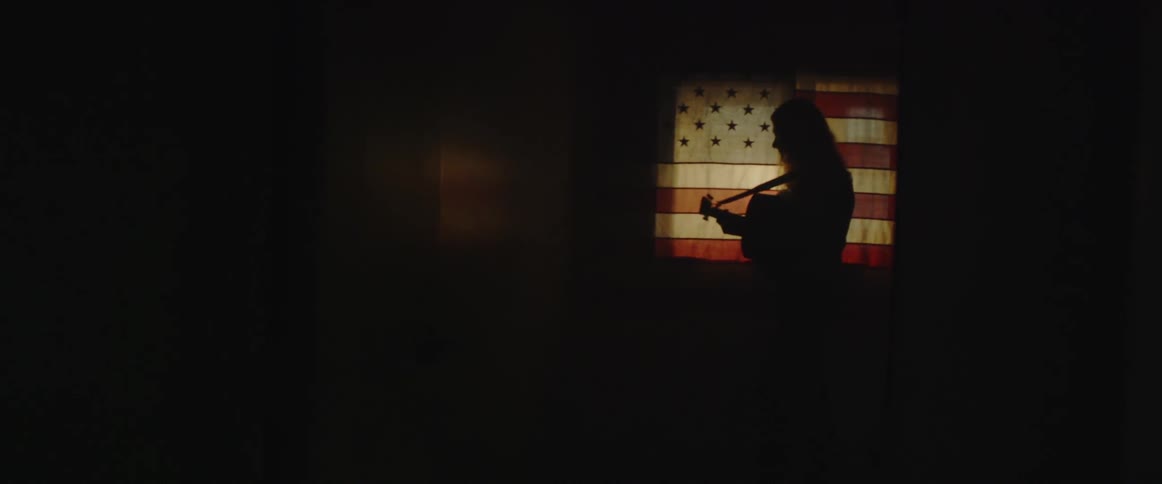 An american flag hangs over a window as a man plays the guitar