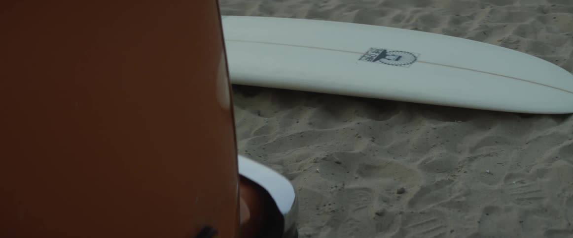A surfboard is lying in the sand near a vehicle in daylight
