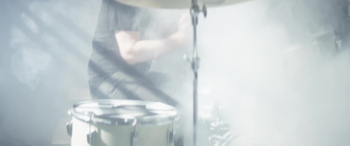 A man plays the drums as dust fills the air