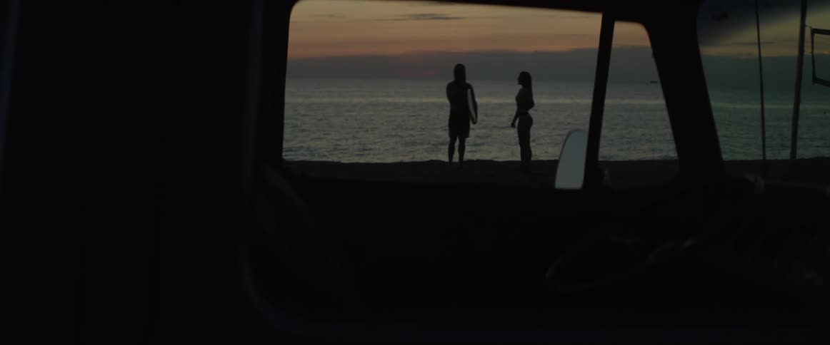 A silhouette of a man and woman standing by the ocean at sunset