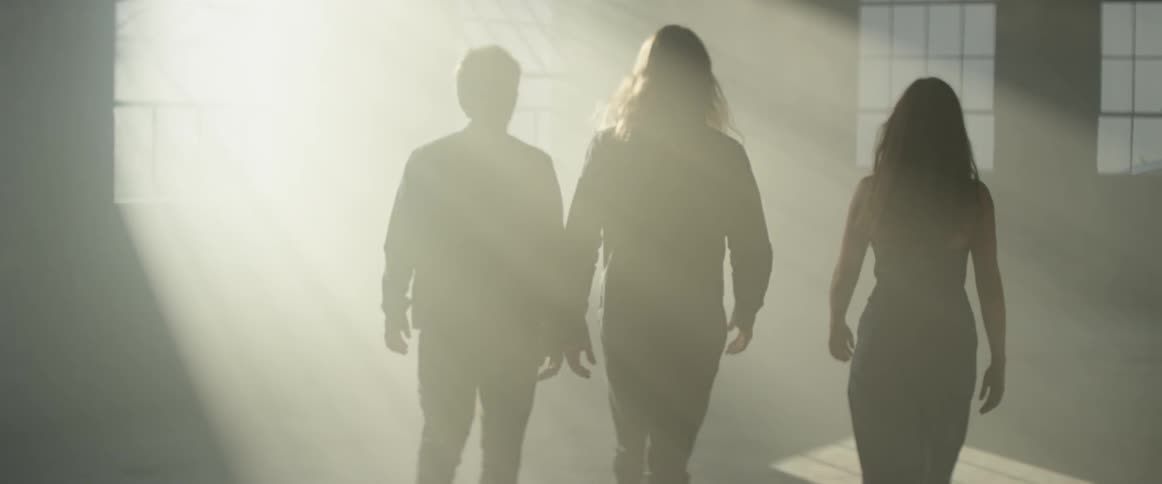 Three people walk through the room as the sun's rays shine on them