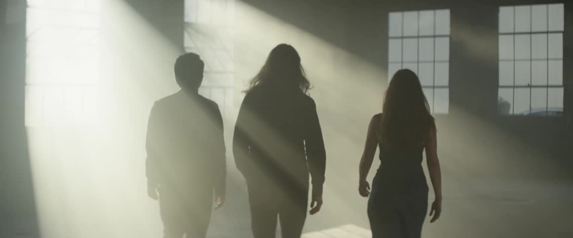 Three people walk in a building as the sun's rays shine on them through a window