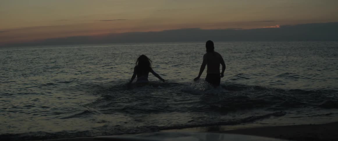 A man and woman run into the ocean and swim at sunset