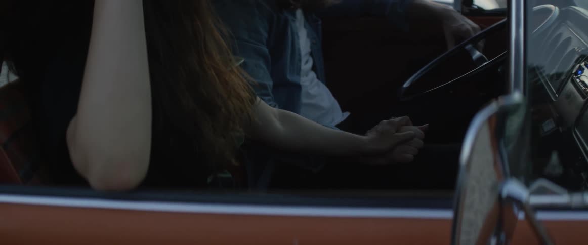 A man and woman hold hands in a car