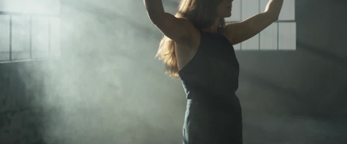 Woman raises her arms over her head as she stands in the rays of the sun