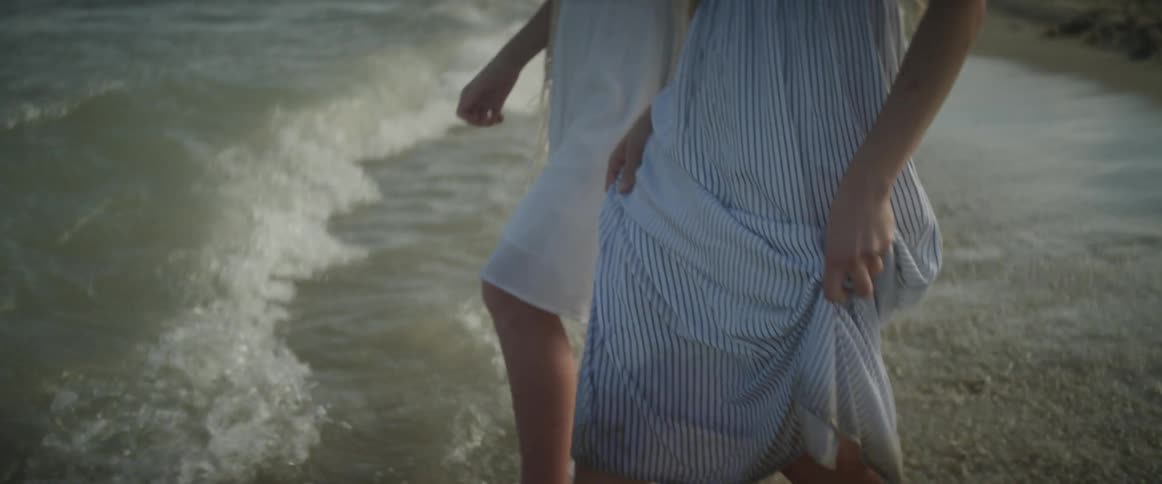 A woman and a girl wade into the surf on a sunny day