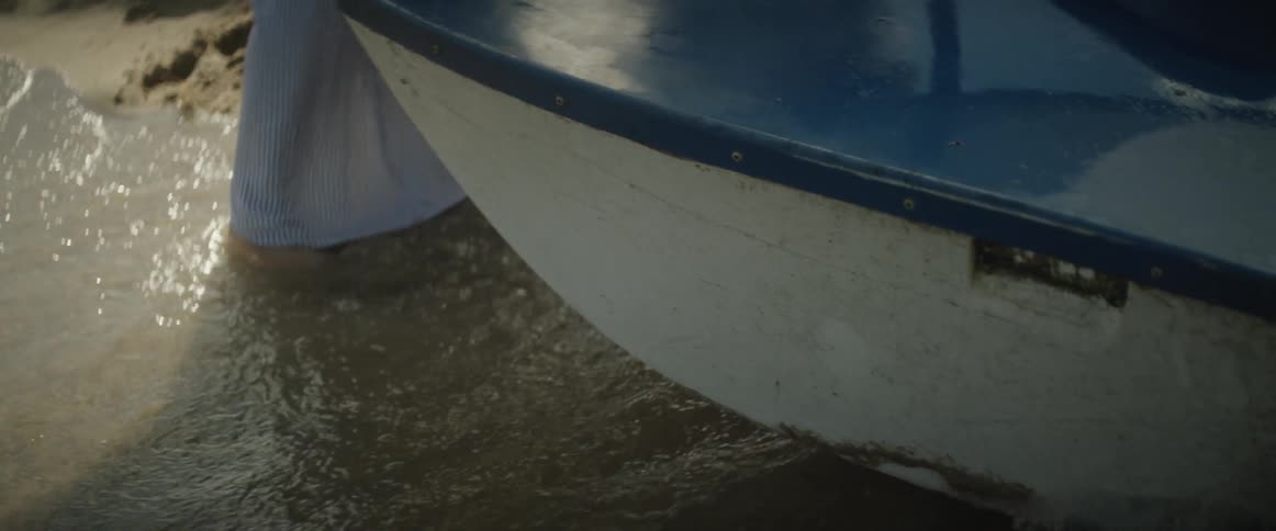 Water rolls in over a man's bare feet as he stands near a boat