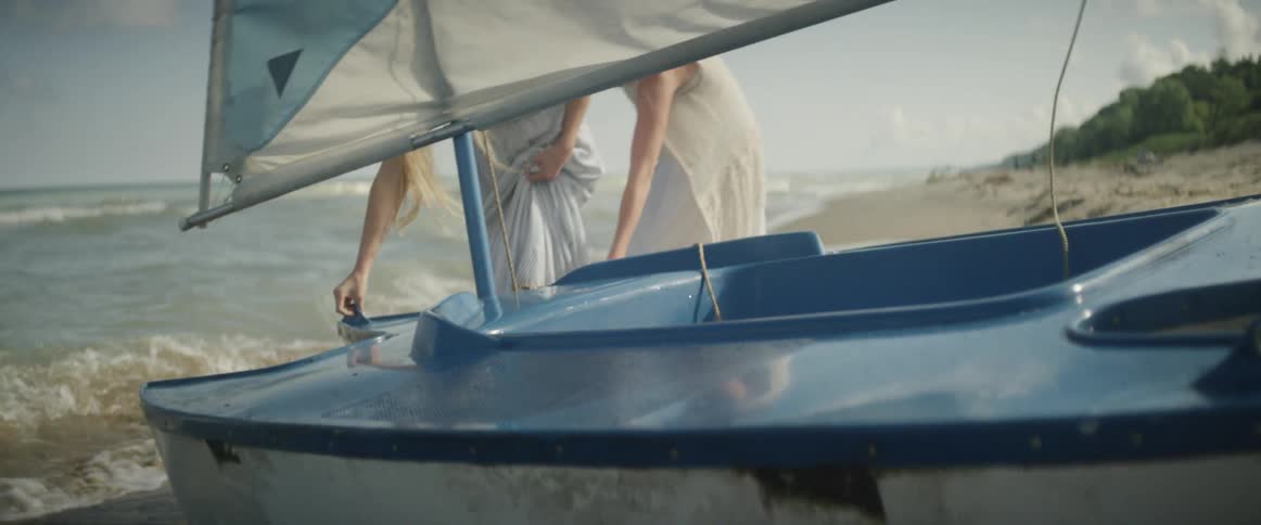 Two girls are towing a sailboat out into the ocean waves in daylight