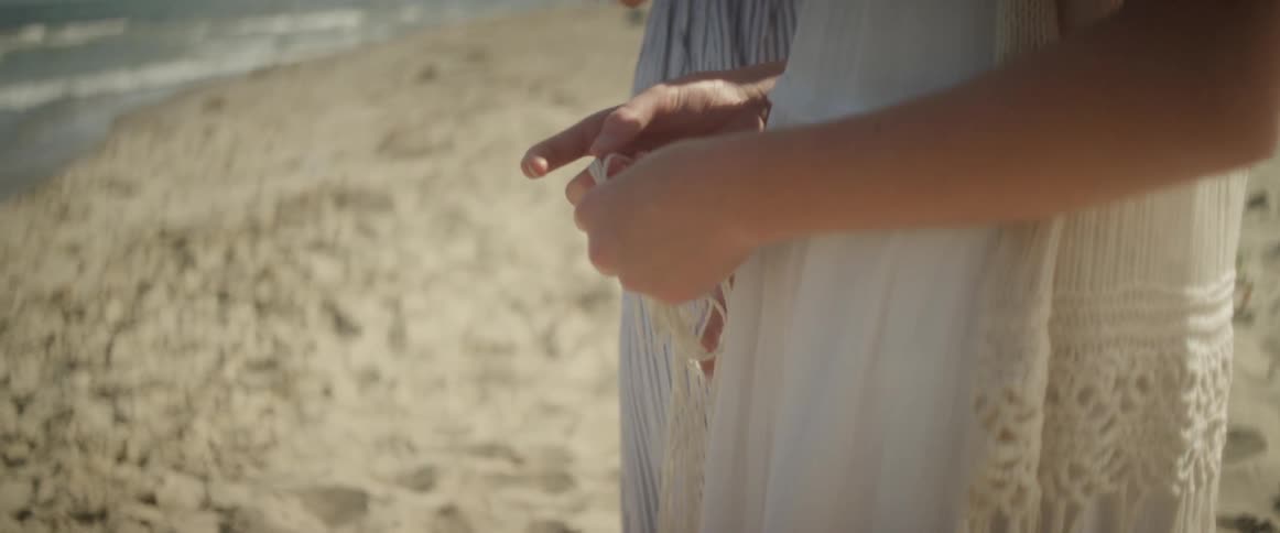 A woman plays with the fringe of her scarf while standing on the beach