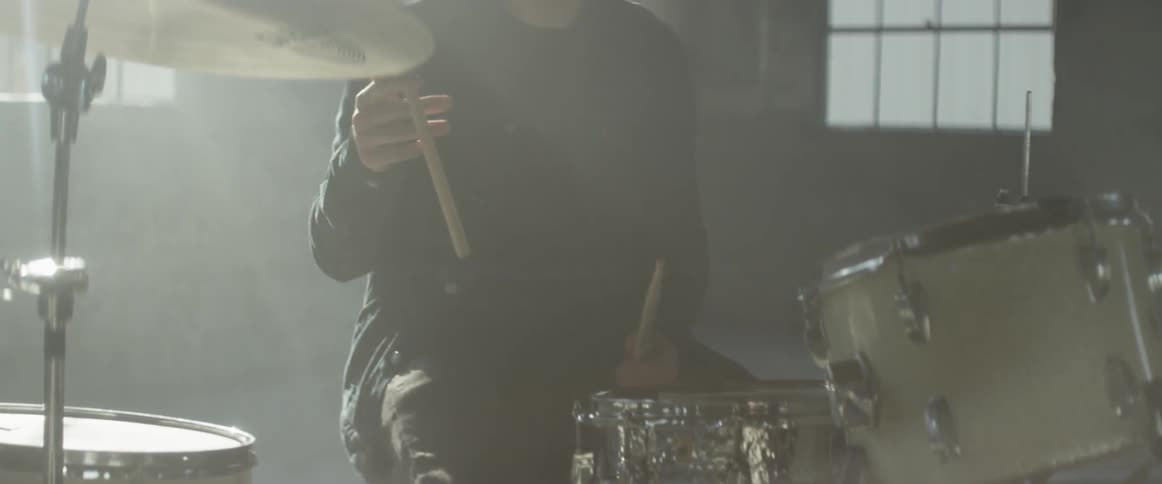 Man sits behind a drum set twirling a drumstick in his hand