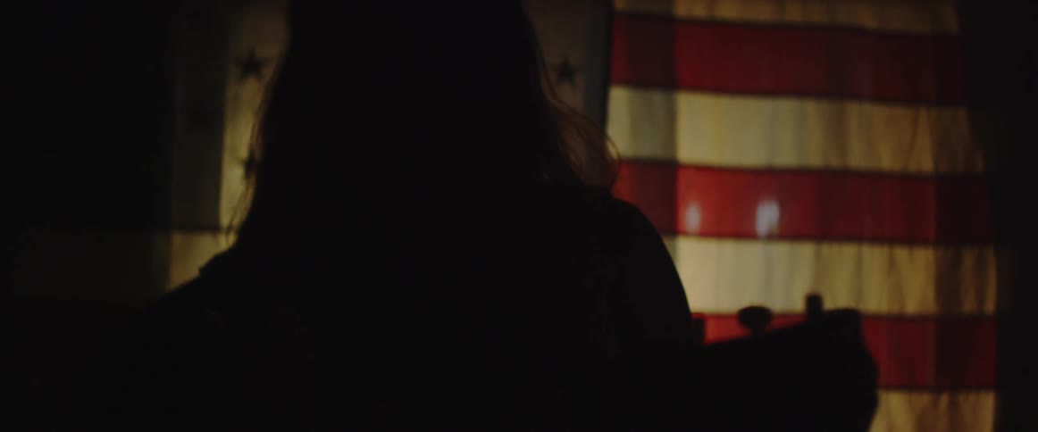 A man plays a guitar in front of a flag covering a window