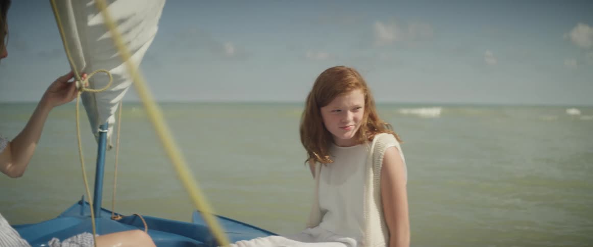 A girl sits on the edge of a sailboat on a sunny day