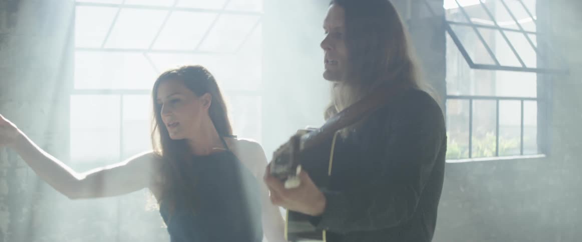 A man plays a guitar and sings with a woman dancing next to him