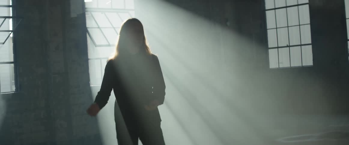 A man is swaying his arms as he stands inside an abandoned building in sunlight