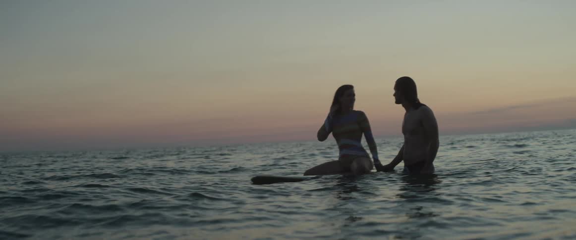 Man and woman surf at sunset