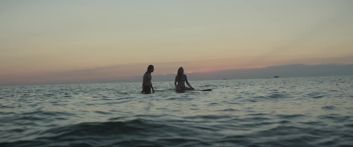 A man and woman wade into the ocean waters