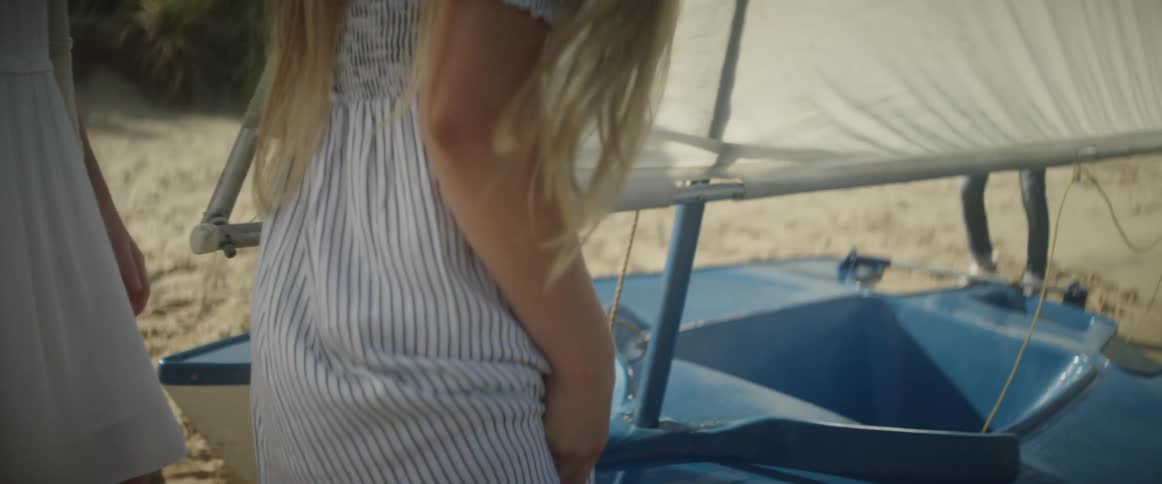 Two women stand beside a small sailboat on the sand