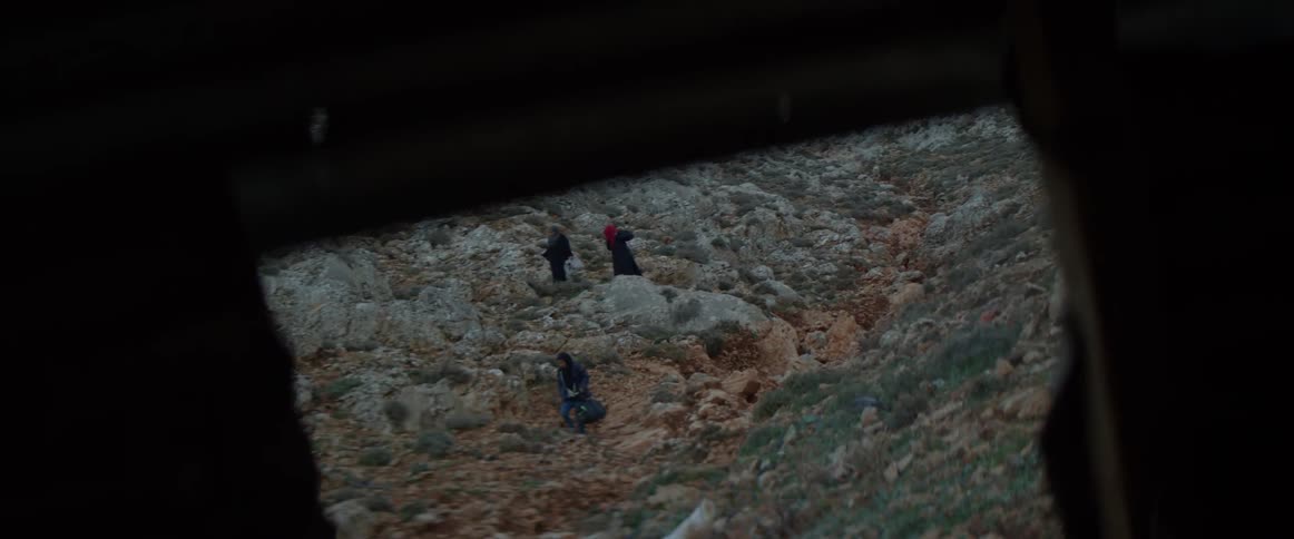 Three people walk across a rocky field at sunset