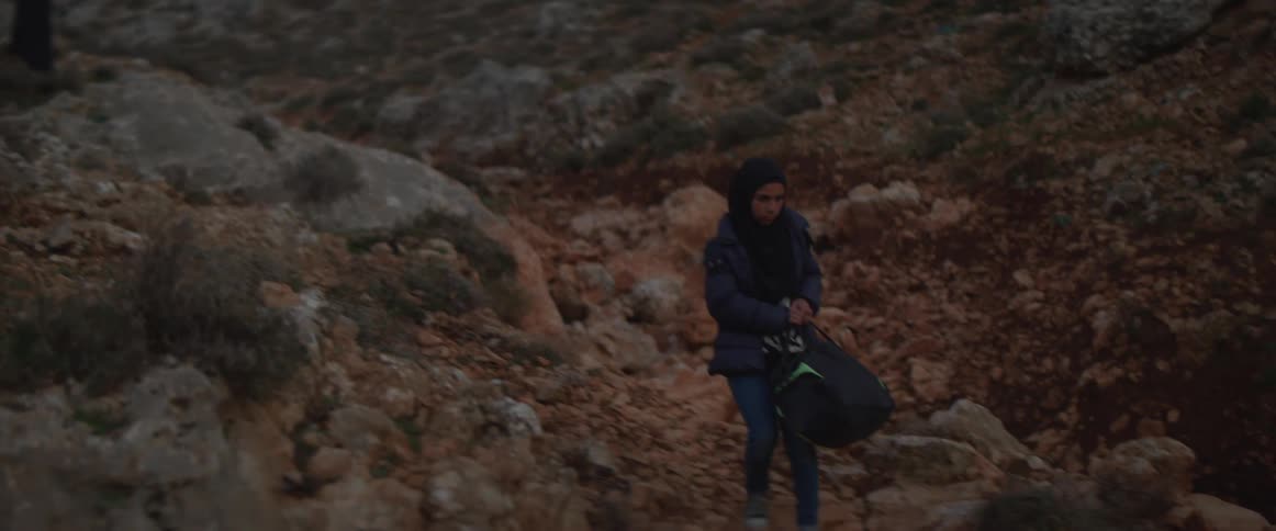 Several people carry bags walking over rocky landscape
