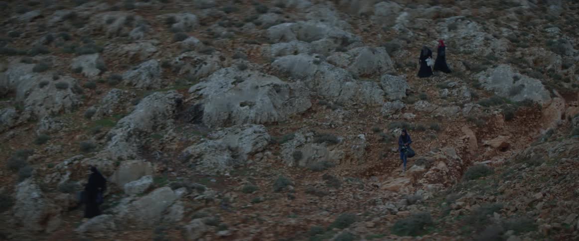 Refugees are crossing a rugged landscape at dusk