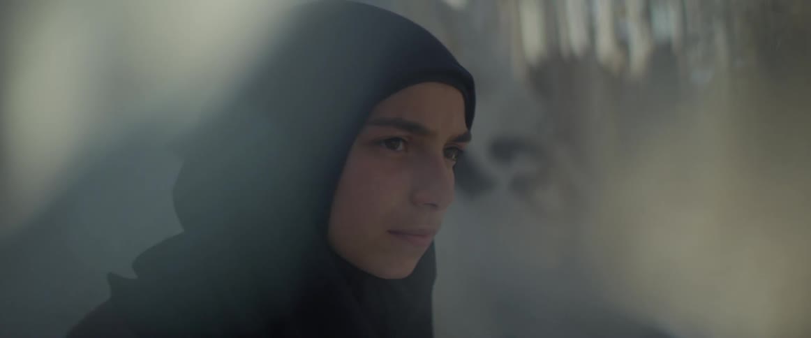 A woman wearing a headscarf looks up from reading a book