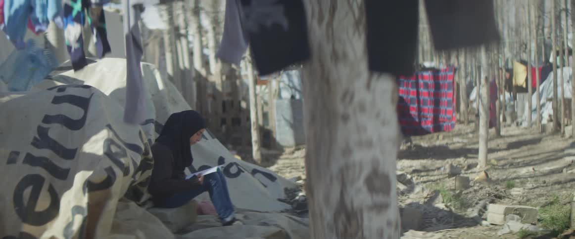 Woman sits outside near a large canvas tent