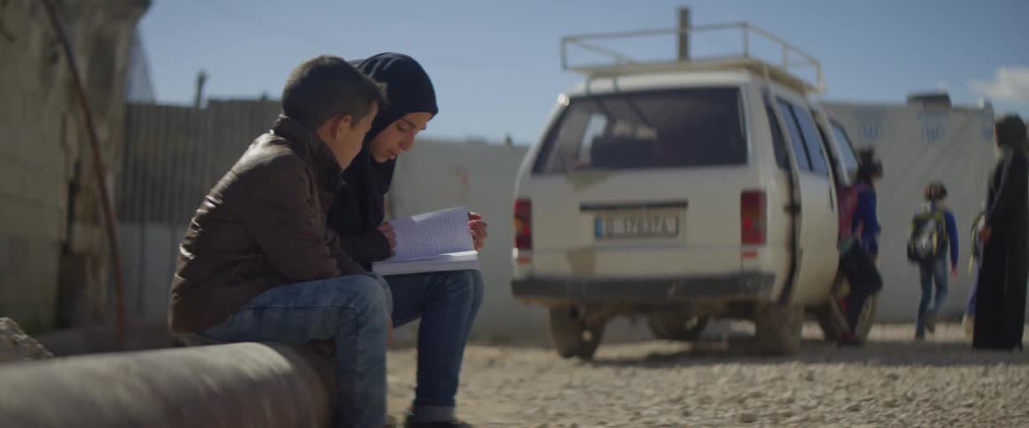 Two children sit outside on a pipe reading a book