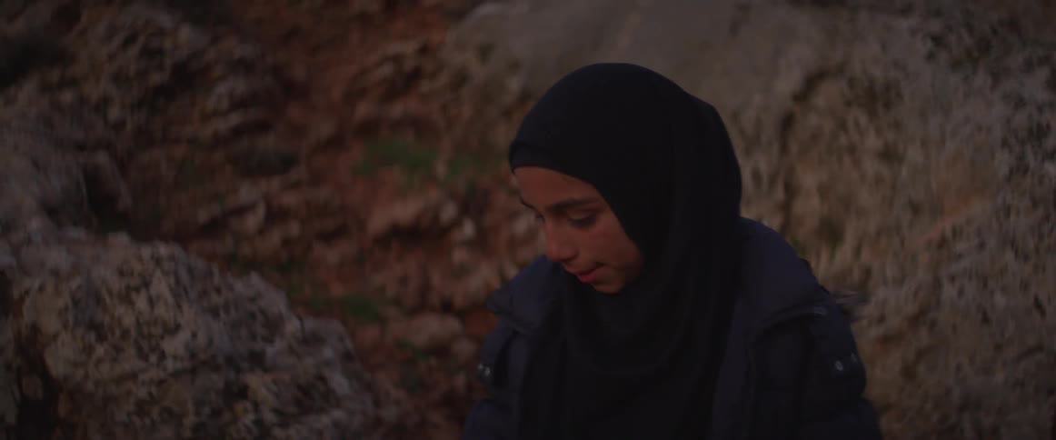 A girl wearing a headscarf makes her way down a rocky slope
