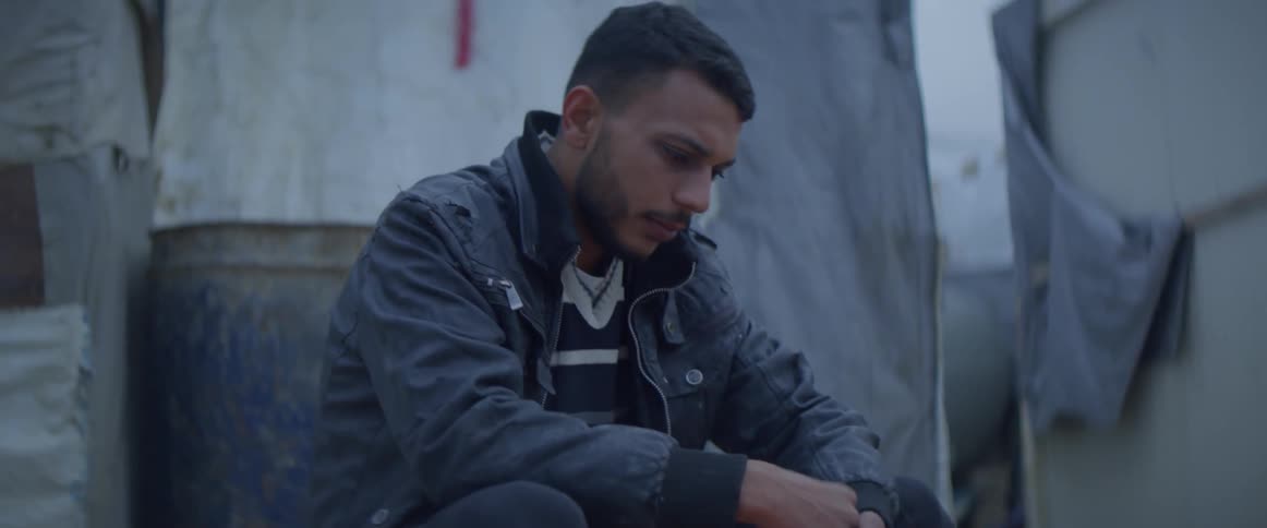 Man warms his hands over a small fire sitting next to a tent