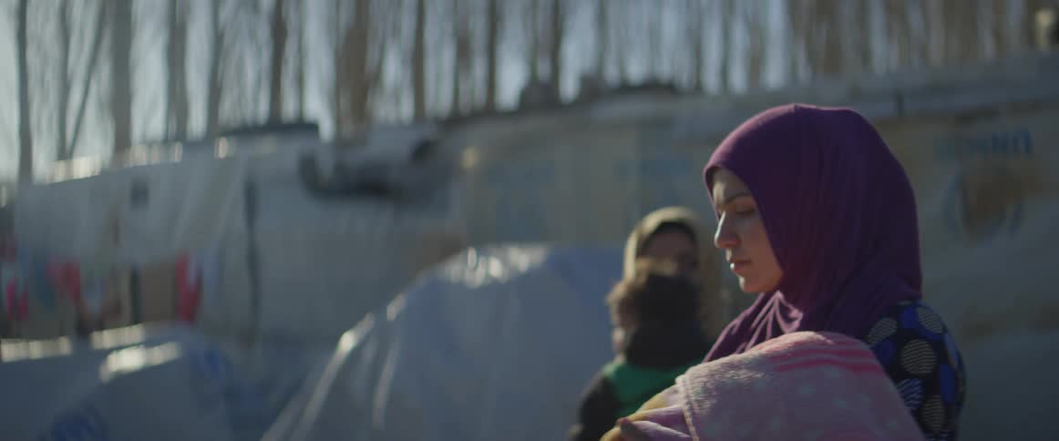 A woman carrying a baby in a blanket walks up to a doctor on a sunny day