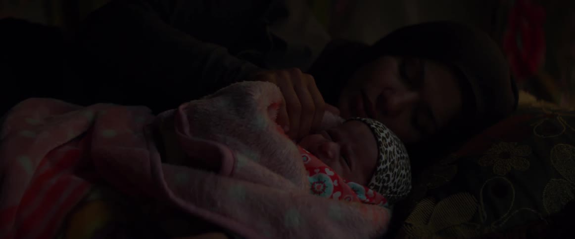 Woman pats a baby wrapped in a blanket as it lays next to her