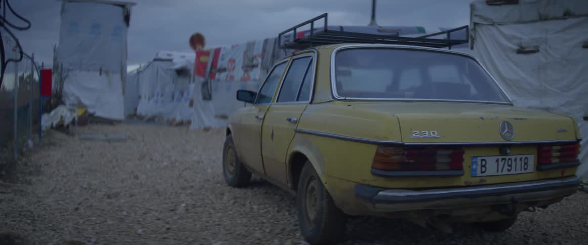 A car is parked near a tent city on a cloudy day