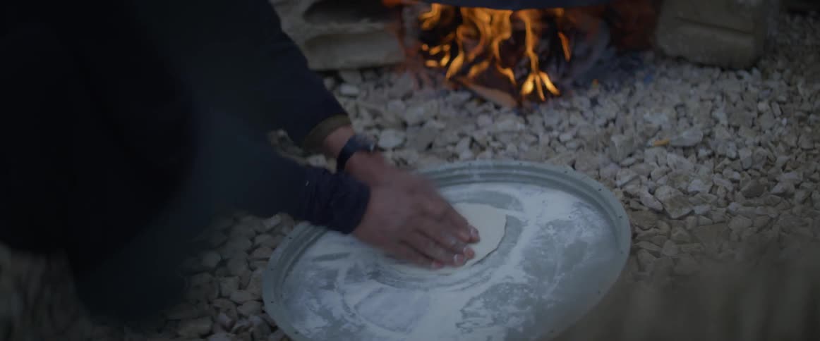 Person prepares flatbread over an open fire