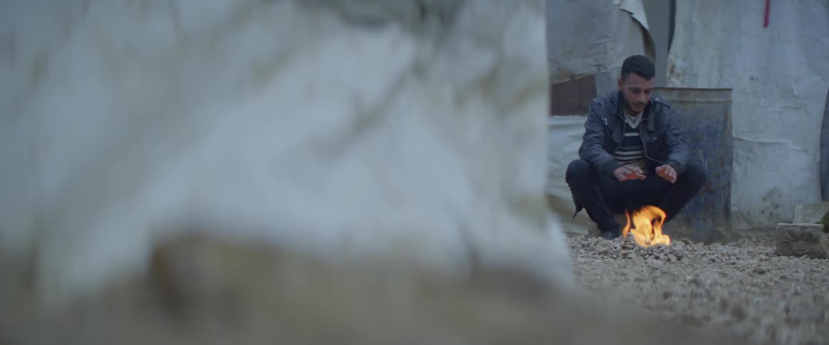 Man sits next to a small fire as he warms his hands