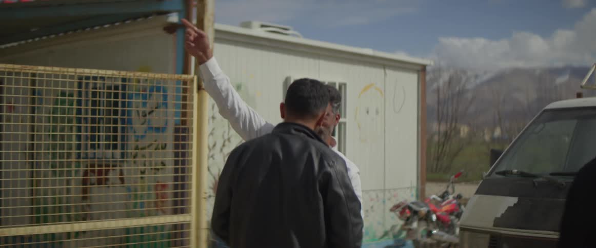 A man waves over another and leads him to a car