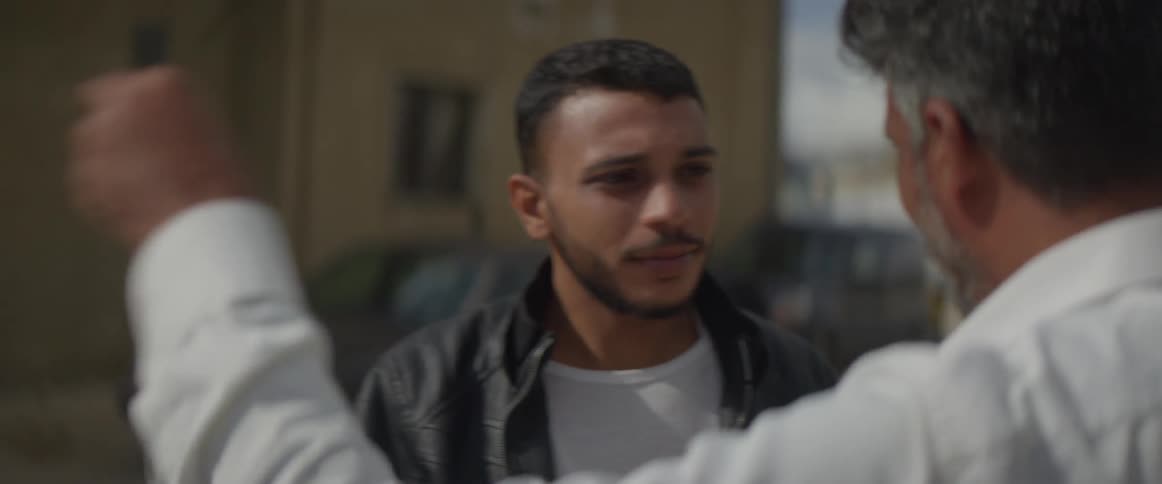 Several people walk in a village and one man talks to another man and gets in a vehicle