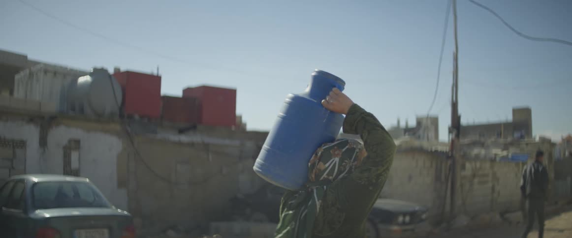 A woman carries a jug on her shoulder as she walks on a village road