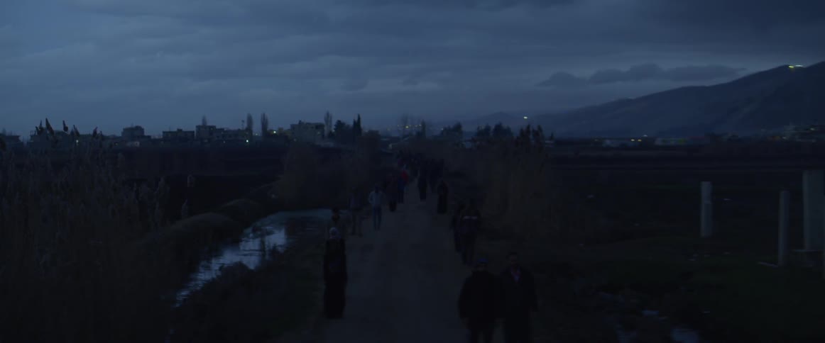 A group of people walk away from a city on a dirt road
