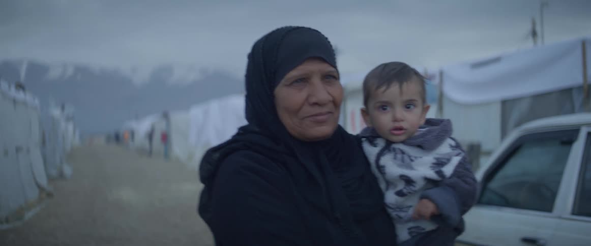 A woman carries a boy on a dirt road in a tent city