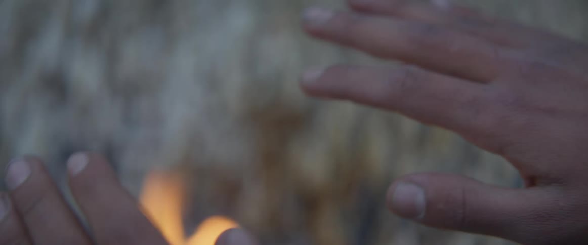 Person warms their hands over a fire outside