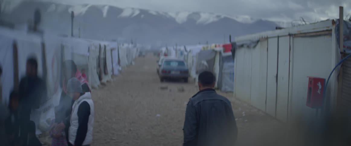 A man is walking through a refugee camp on a winter day