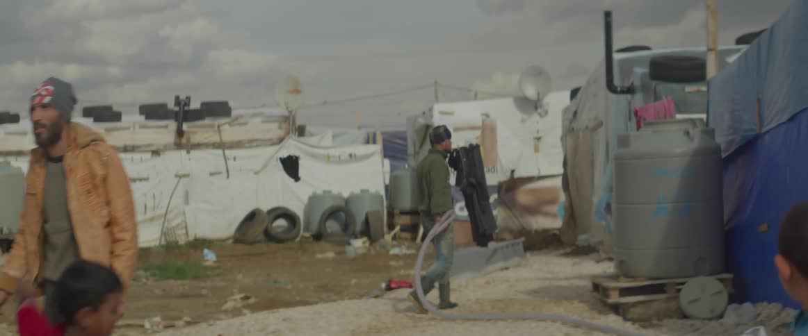 People walk and children play on a road in a tent city