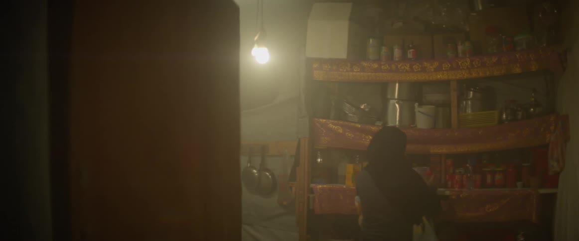 A woman carrying a baby walks into a store room looking for something on a shelf